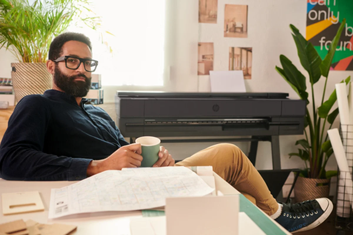 Arquitecto con un café revisando planos junto a un plotter HP DesignJet en su estudio