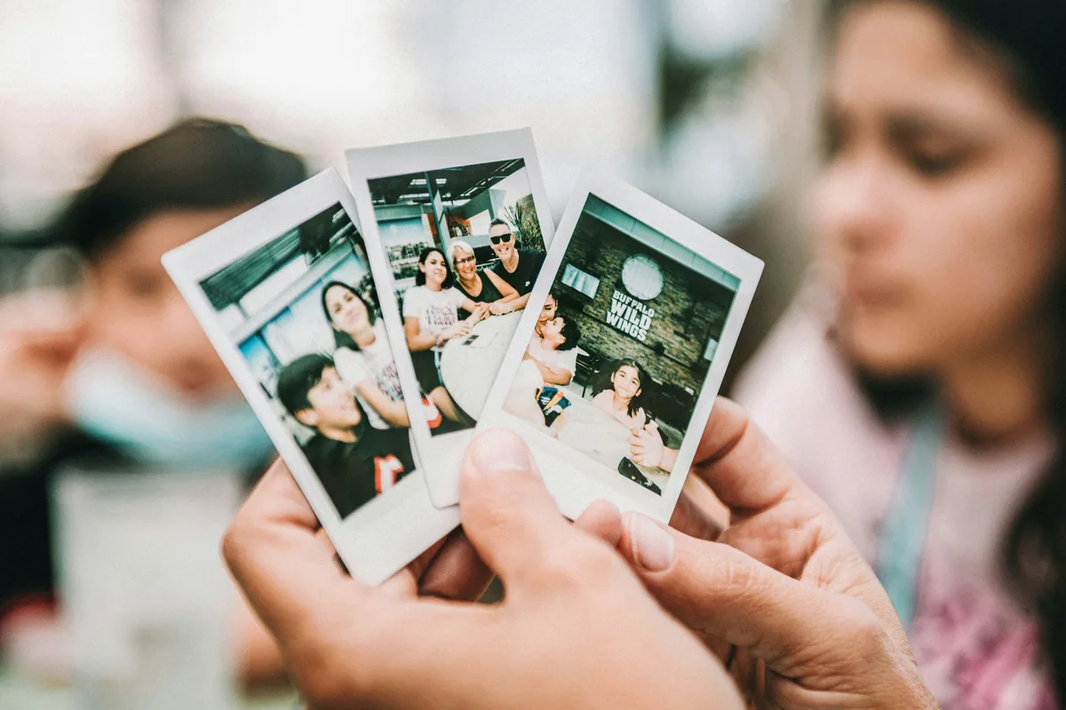 Una mano sujeta tres copias Instax recién reveladas con fotos de familia