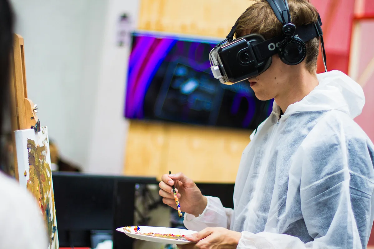 Un joven con un visor de realidad virtual pinta sobre un lienzo mientras sostiene una paleta de colores